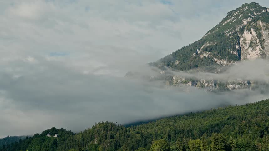 Wispy clouds drift across the forested slopes of a majestic mountain