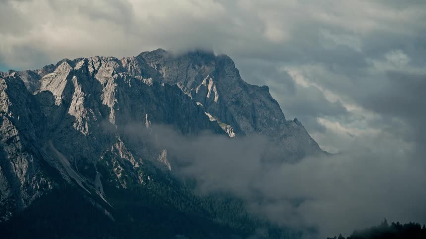 A dramatic timelapse captures clouds and mist swirling around the rugged peaks of a mountain range