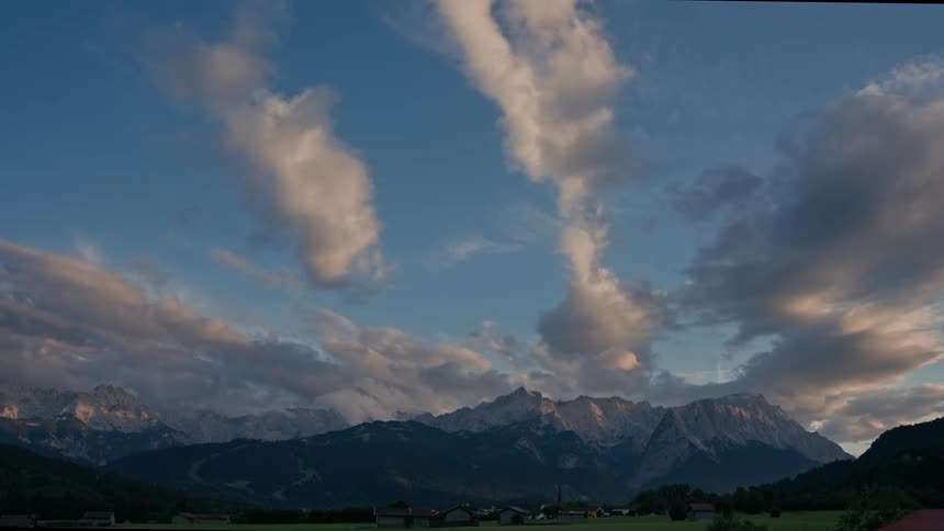 A stunning day-to-night timelapse of clouds passing over the majestic Alps, transitioning from a bright blue sky through a colorful sunset into the deep dark of night