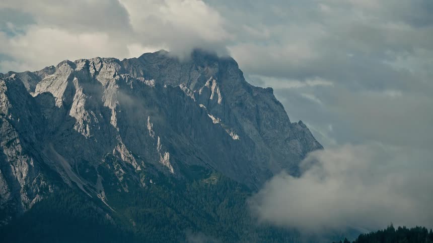 A majestic shot captures a rocky mountain peak partially obscured by slow-moving clouds