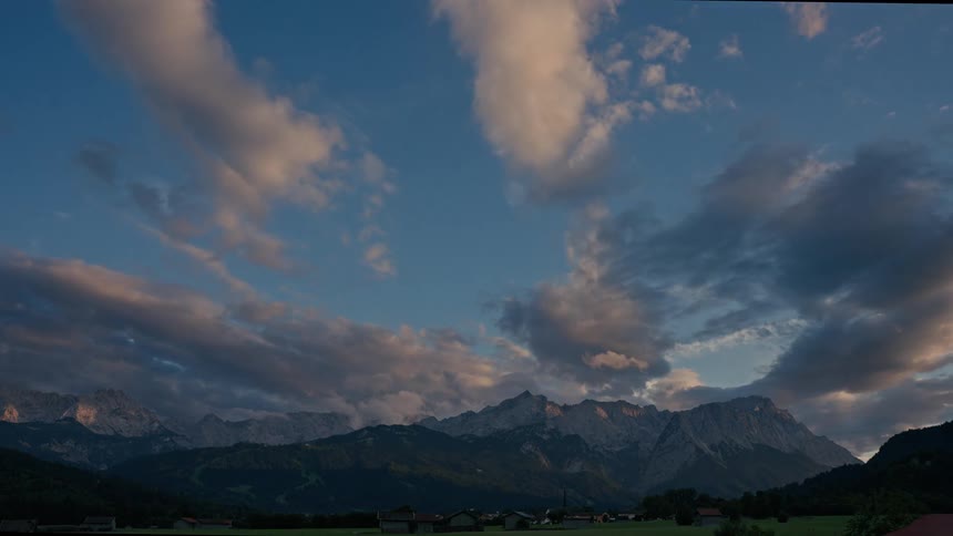 A serene timelapse captures clouds drifting over a majestic mountain range during a picturesque sunset