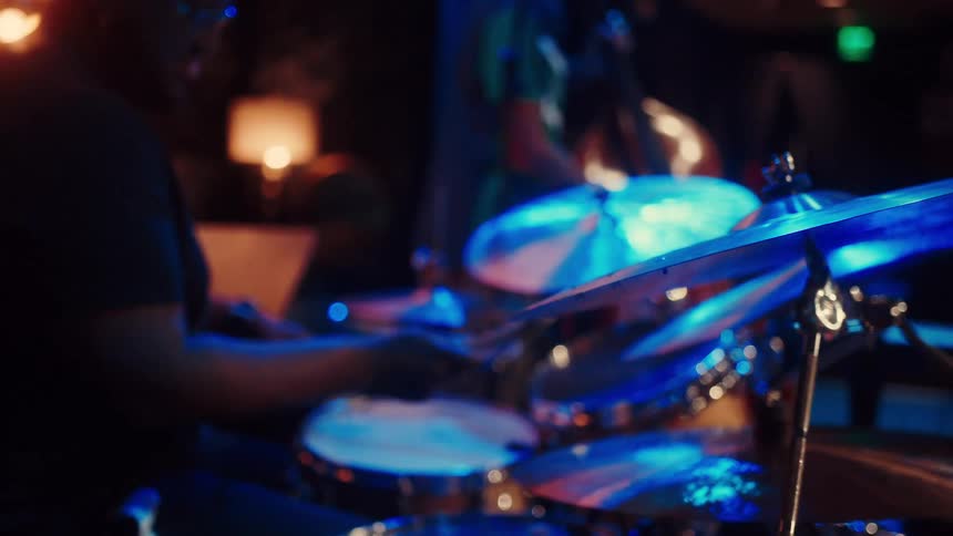 Atmospheric slow motion close-up of a drummer playing a drum kit under dramatic blue stage lights during a live performance