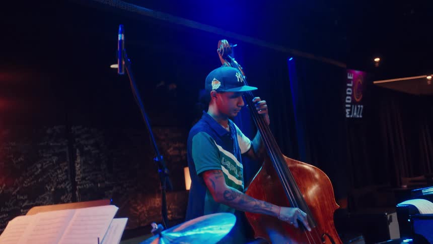 A focused bassist with tattoos plays his double bass under cool blue lights during a live jazz performance