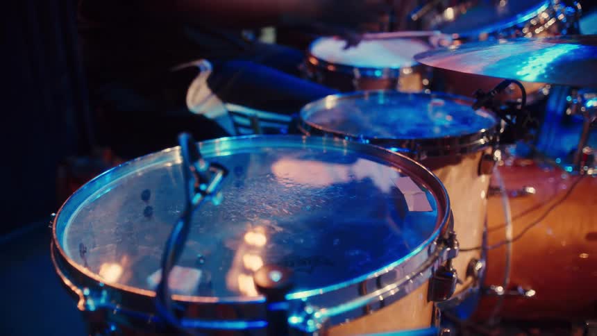 A close-up shot of a tom-tom drum under blue stage lights as a drummer performs in the background