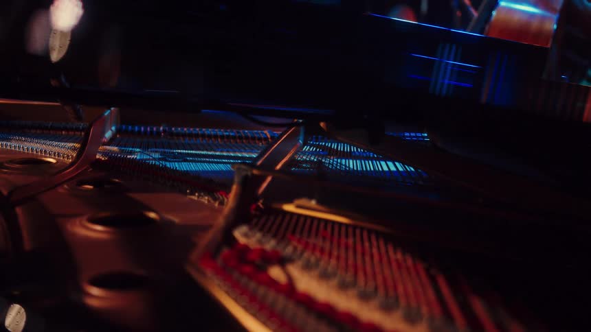 A slow and artistic dolly shot reveals the intricate strings and mechanisms inside a grand piano, illuminated by moody blue and warm stage lights
