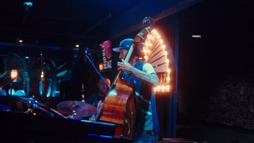 A bassist and drummer perform live jazz music on a dimly lit stage in a club