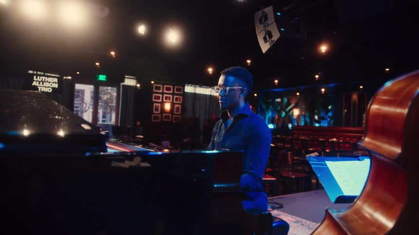 A sophisticated pianist plays the grand piano on stage in a dimly lit, atmospheric jazz club