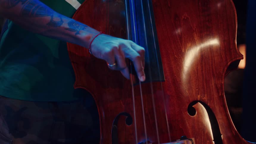 Close-up of a tattooed musician's hand skillfully playing a beautiful wooden double bass during a performance