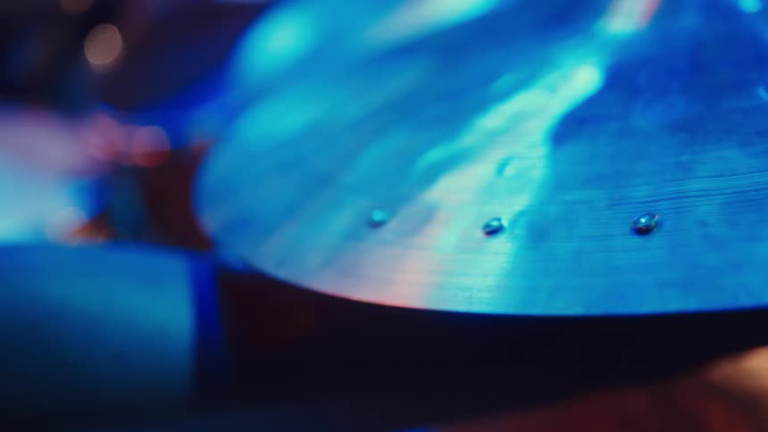 A close-up rack focus shot of a drum set's cymbals under vibrant blue and pink stage lights