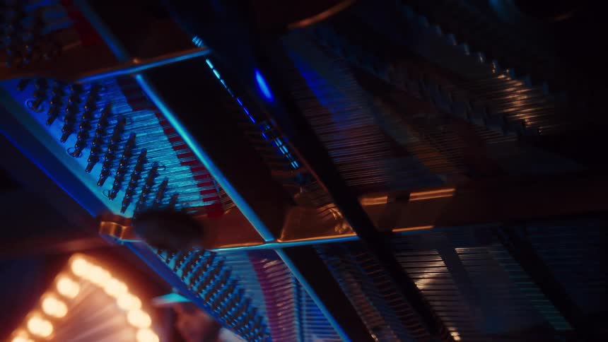 Abstract close-up of the hammers and strings inside a grand piano with dramatic blue lighting during a performance