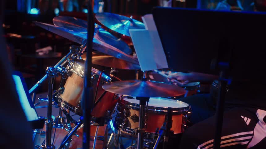 A skilled drummer plays a lively beat on his drum kit on a dark stage with vibrant blue lighting during a live music performance
