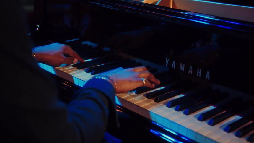 A pianist's hands gracefully play a Yamaha grand piano in a dimly lit room with blue ambient lighting