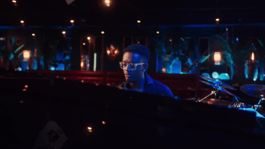 A talented Black pianist passionately sings and plays the grand piano during a jazz performance in a dimly lit, atmospheric club