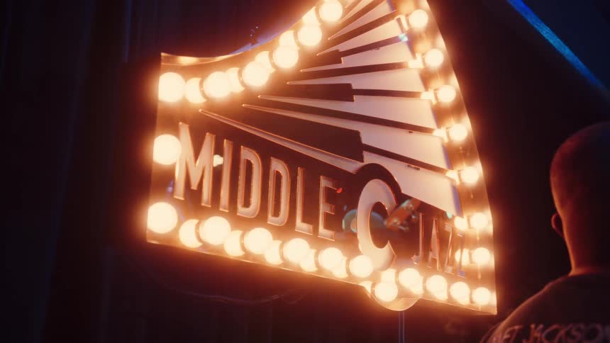 A whimsical puppet with a green hat playfully peeks through the glowing marquee sign of the 'Middle C Jazz' club