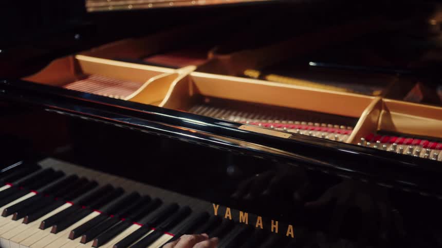 A musician's hands glide across the keys of a beautiful black Yamaha grand piano in a softly lit, intimate setting