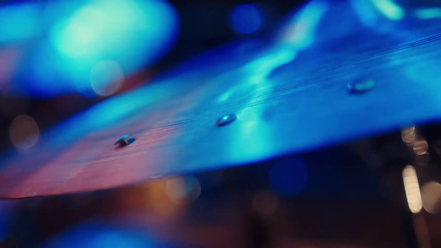 Slow-motion macro shot of water droplets dancing on a vibrating cymbal under cool blue stage lights