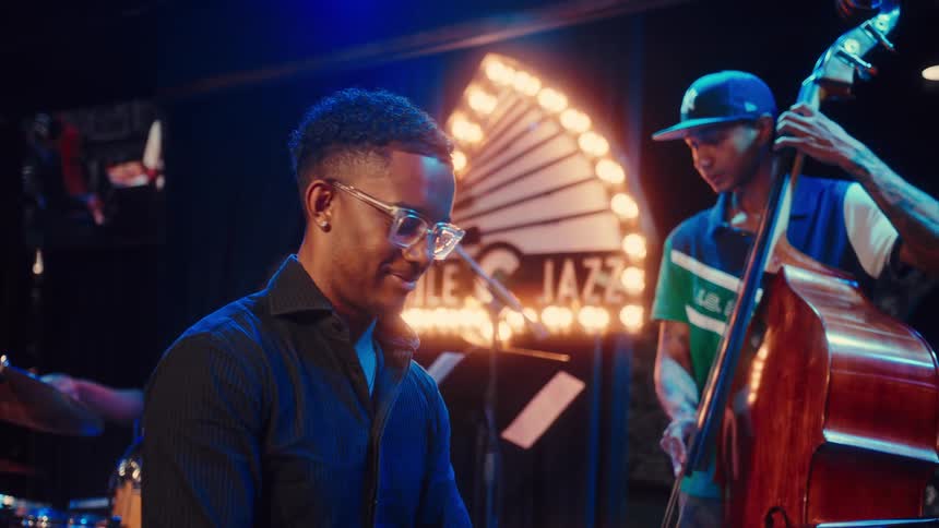 A talented pianist in glasses focuses intently on playing a grand piano during a soulful live performance with his jazz band