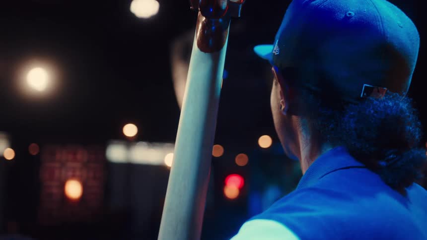 An intimate, over-the-shoulder close-up of a bassist in a baseball cap playing a stand-up bass on a dimly lit stage with cool blue lighting