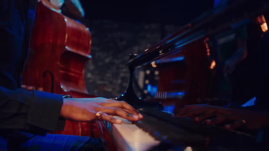 A talented pianist's hands move gracefully across the keys of a grand piano during a live jazz performance in a dimly lit club
