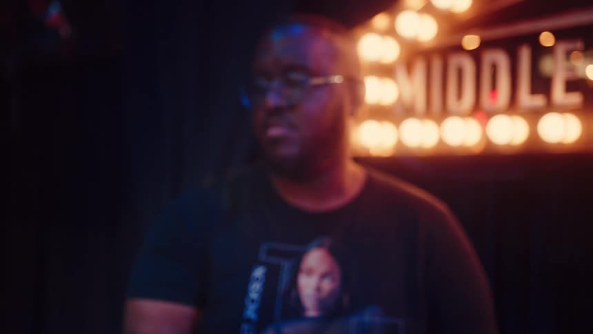 An artistic rack focus from a shimmering cymbal reveals a passionate drummer playing on stage at a music venue