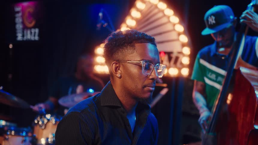 Close-up on a stylish young pianist performing with his band in a cool, atmospheric jazz club