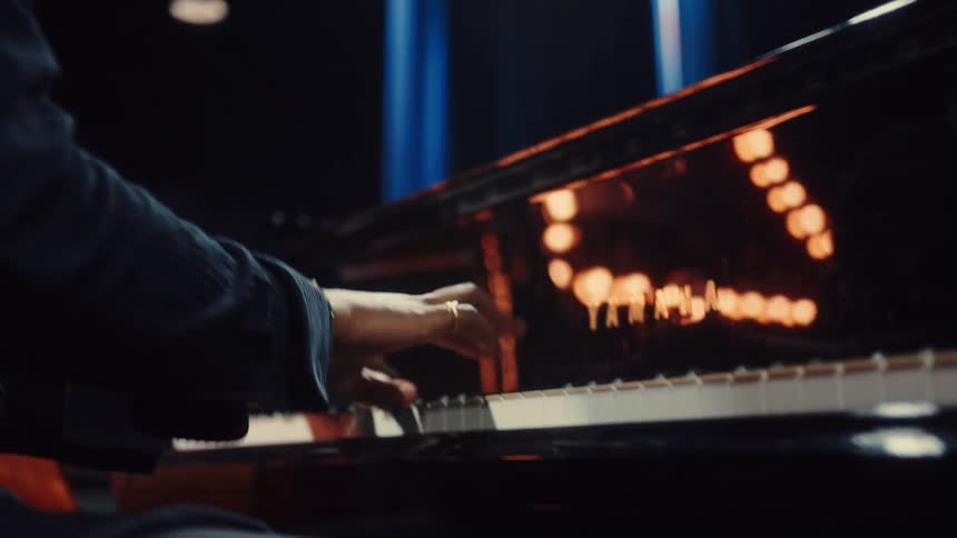 Close up slow motion of a man's face and hands playing a Yamaha grand piano in a dark room with spotlights