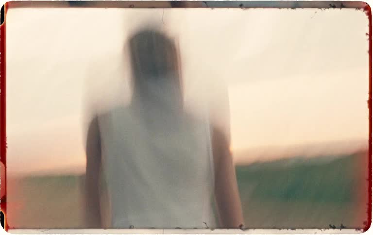Shaky and blurry vintage-style footage captures a woman running through a field of trees before the camera spins wildly