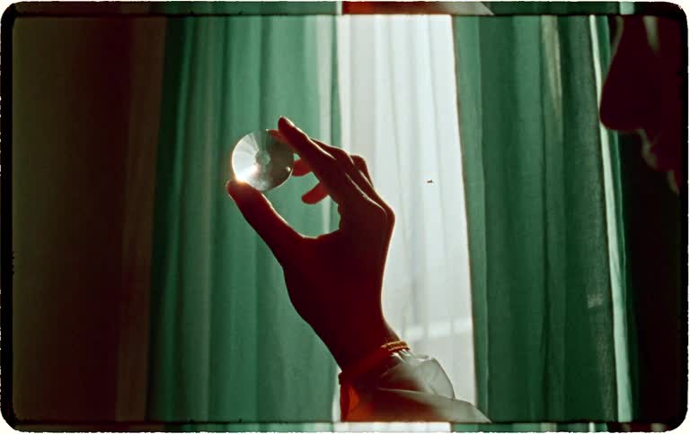 A hand holds a faceted crystal up to a window, admiring the way the light catches and refracts through it