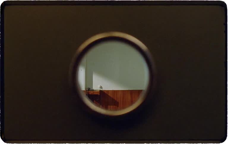 Voyeuristic perspective through a door's peephole captures a young girl inside a vintage-style room