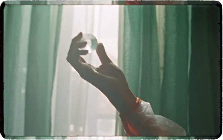 A mysterious hand in a retro outfit holds a faceted crystal up to the light of a window with green curtains