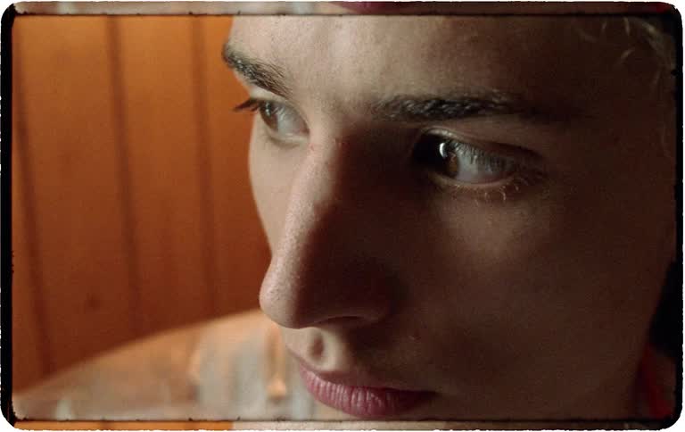 A thoughtful young person in a vintage-style room curiously examines a small crystal prism in the soft light from a window