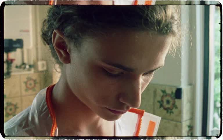 Vintage film-style close-up of a somber young person dressed as a nurse in an old-fashioned kitchen