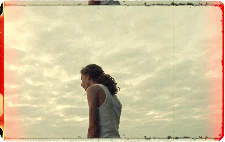 Vintage 8mm footage shows a young man running out of a dense forest to watch the sunset over a vast landscape