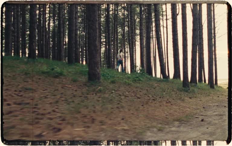 A vintage-style tracking shot follows a man as he runs through a dense forest of tall pine trees