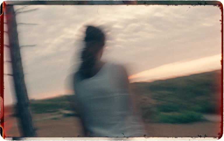 Dreamlike, vintage-style footage captures a person running frantically through a desolate forest at sunset, ending in a disorienting spin