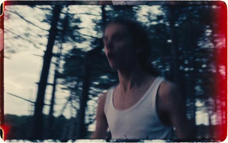 Vintage-style handheld footage shows a panicked young man running through a dark forest at twilight