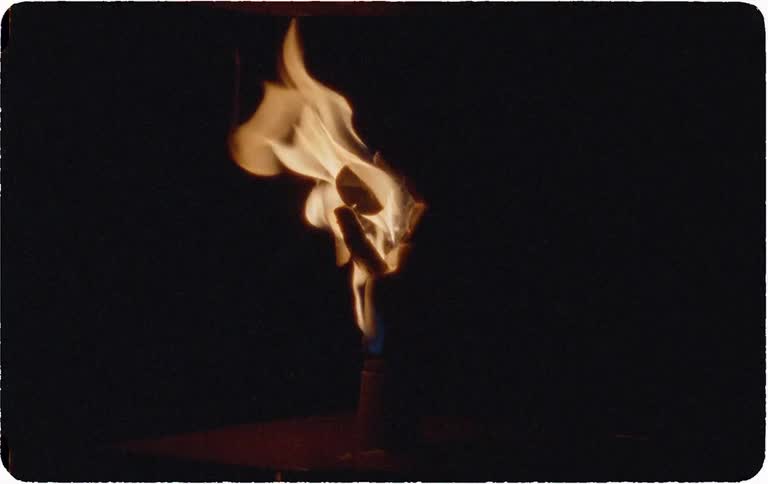 A close-up slow-motion shot of a single flame from a torch flickering against a dark background, captured on vintage film