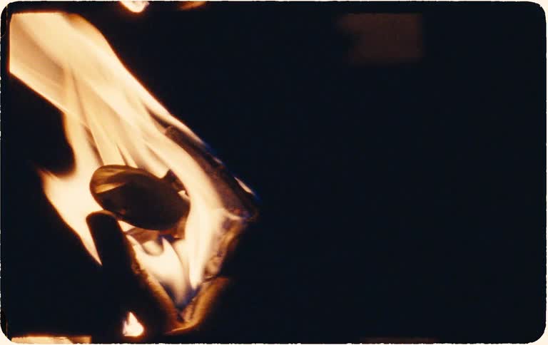 A strip of paper burns from the bottom up in a dramatic slow-motion close-up with a vintage Super 8 film look