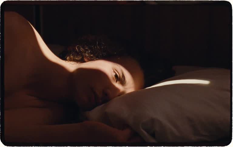 Sunlight falls on a sleeping person's face as they slowly wake up in the morning and turn over in bed