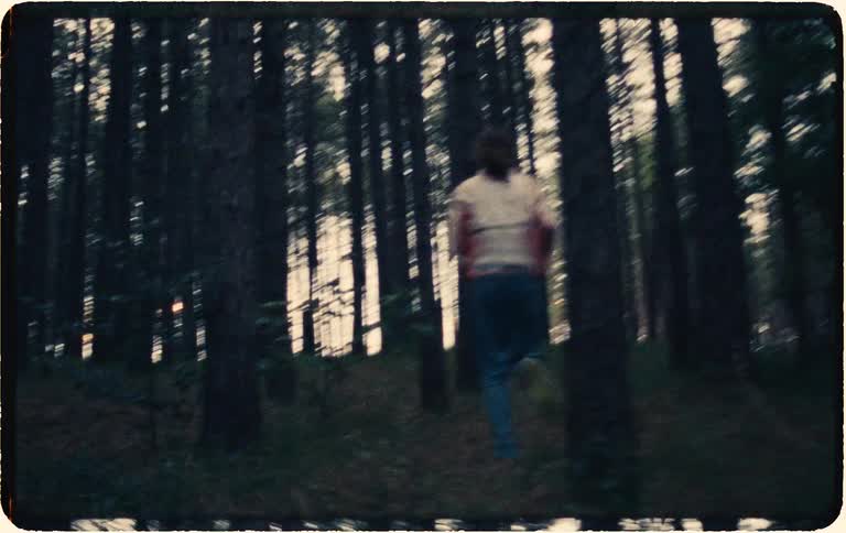 A vintage handheld shot follows a person running in fear through a dark and mysterious forest