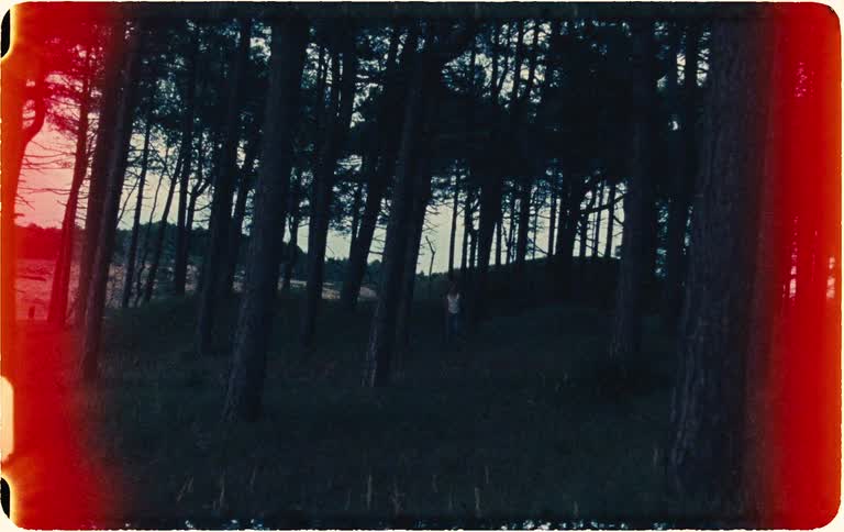 Eerie vintage Super 8 footage shows a frightened young woman running through a dark, spooky forest at night