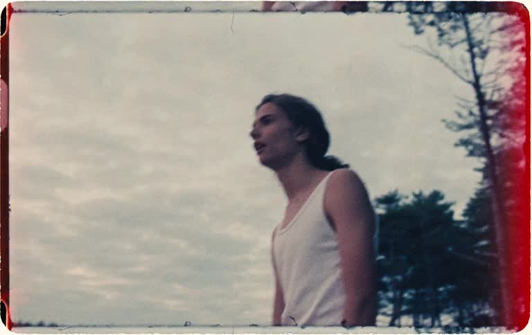 Vintage 8mm footage captures an emotional young man shouting into the twilight sky in a desolate landscape of dunes and trees