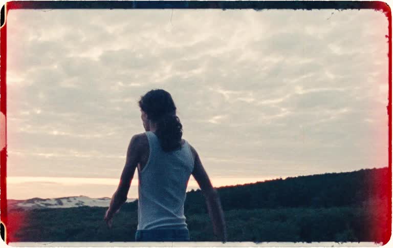 Vintage-style handheld footage shows a panicked young man running out of a dark forest to a coastal clearing at twilight