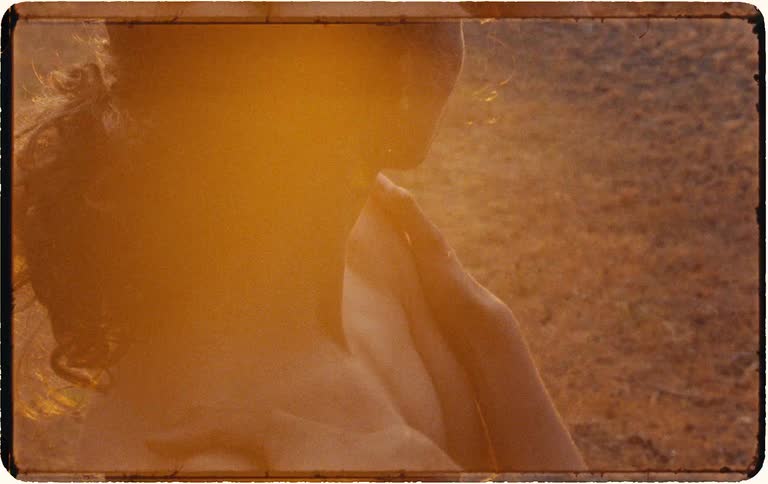 Introspective close-up of a woman's bare back and shoulder as she gently touches her skin in the warm light of golden hour