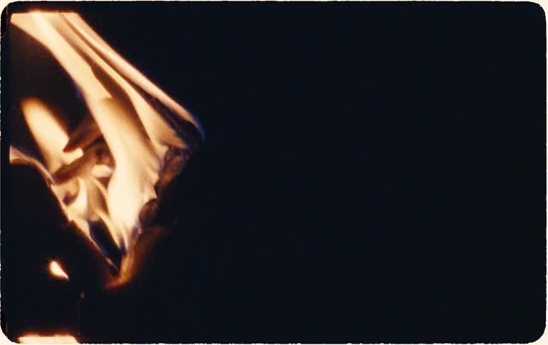 Slow-motion close-up of a piece of paper burning away to nothing against a black background, with a vintage film look