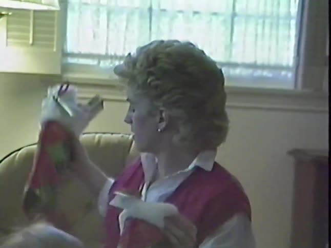 A mother sits with her baby on her lap and checks the presents in her Christmas stocking in this vintage VHS footage