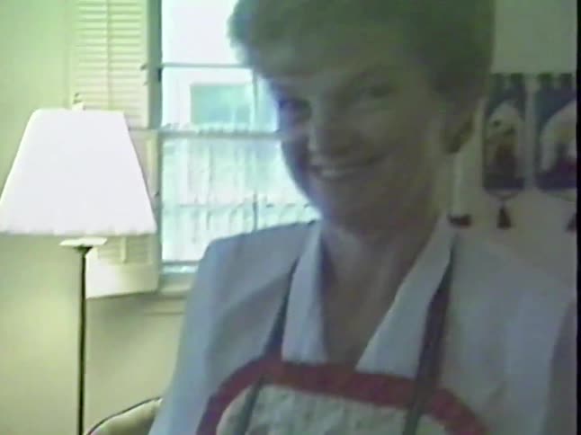 A woman and a toddler play on the living room floor as the camera pans to reveal a smiling grandmother in a chair