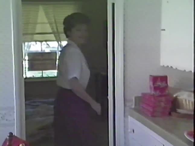 A woman with short hair smiles warmly for the camera while standing in a doorway at home