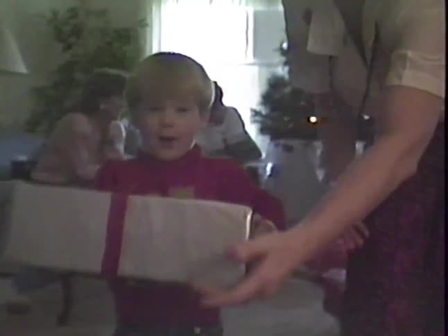 A nostalgic home video from the 1980s shows an excited young boy receiving a Christmas present from his family