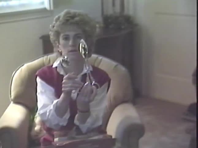 A woman opens a gift of silver serving utensils in a living room, an authentic moment from a 1980s home video